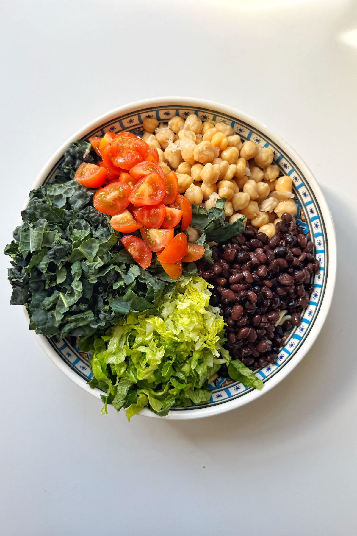 Adding lettuce and fresh ingredients to pasta salad with beans.