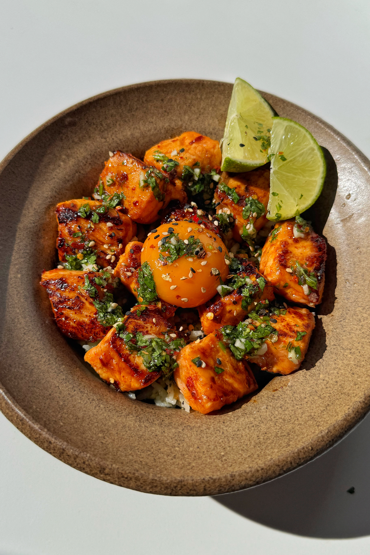 Avocado rice bowl with salmon bites and lime wedges.