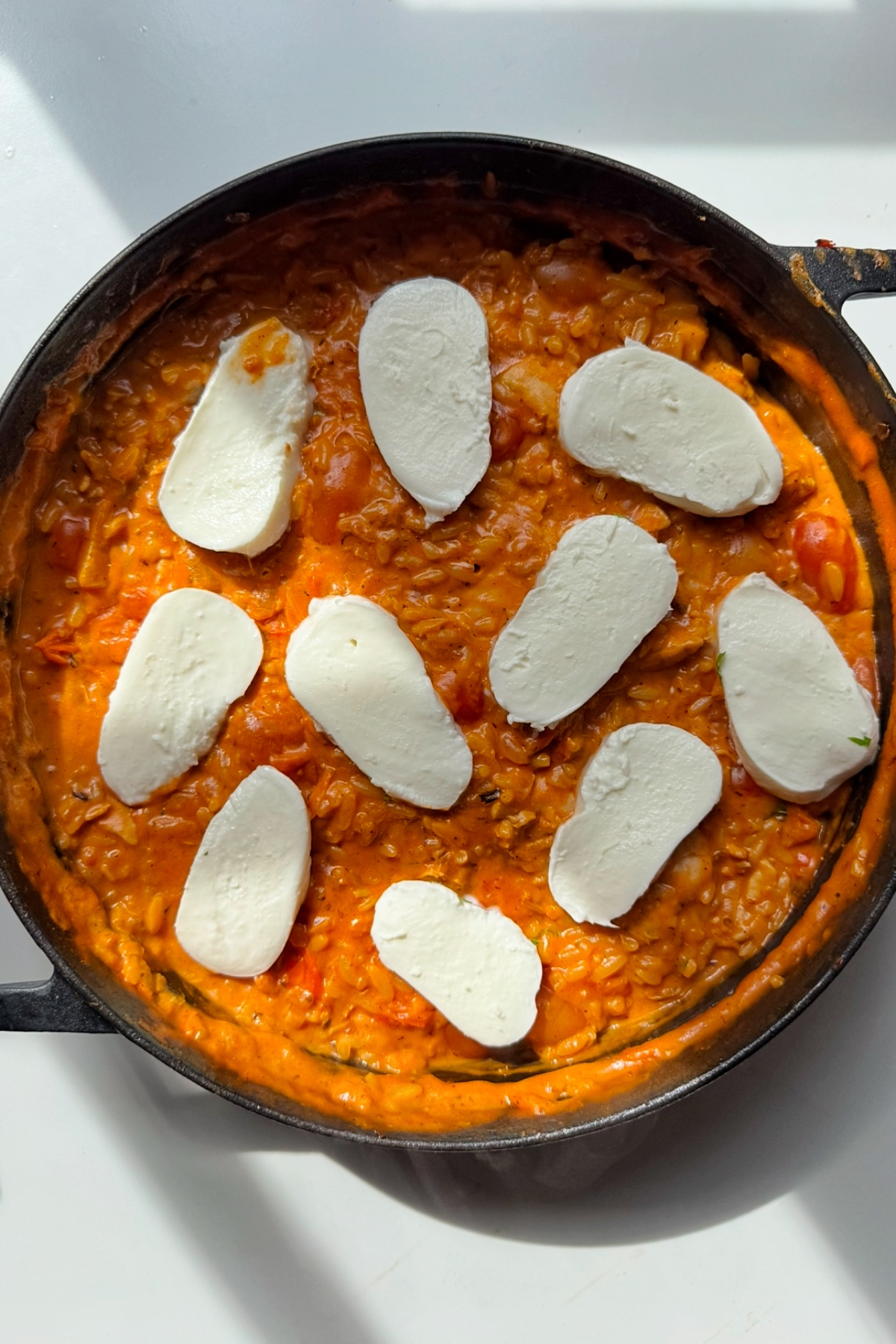 Adding mozzarella slices on top of the creamy chicken orzo.