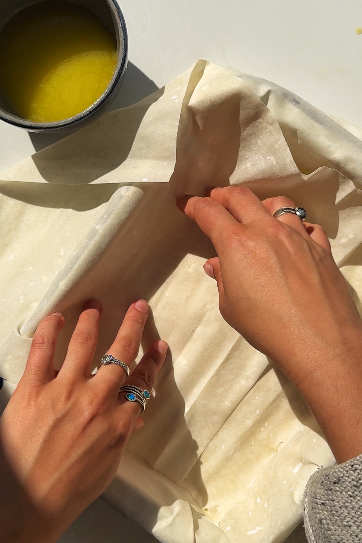 Buttering the base of the pan and adding the filo pastry sheets.