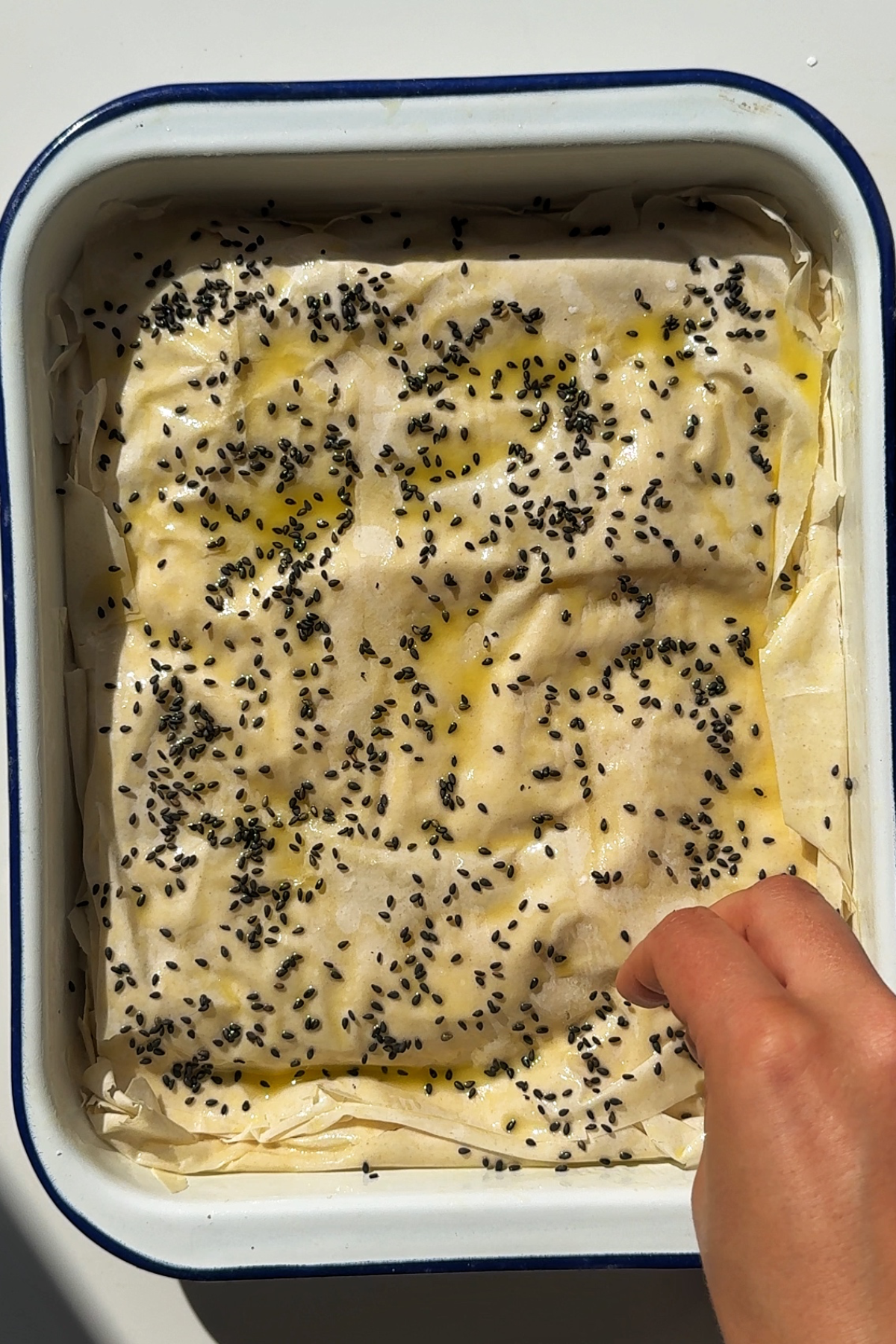 Sprinkling the tiropita with sesame seeds.