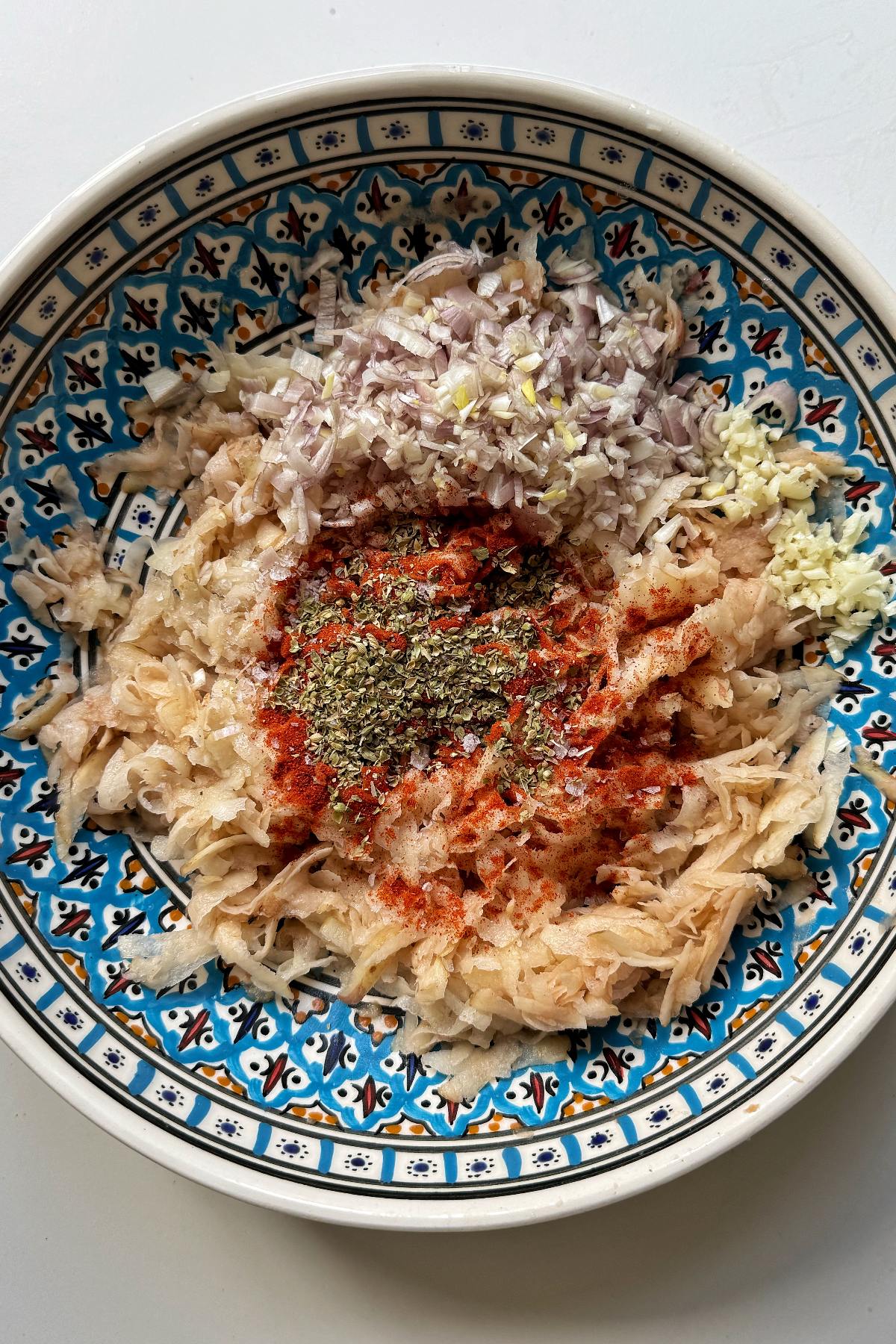 Grated potato with seasonings in a bowl.