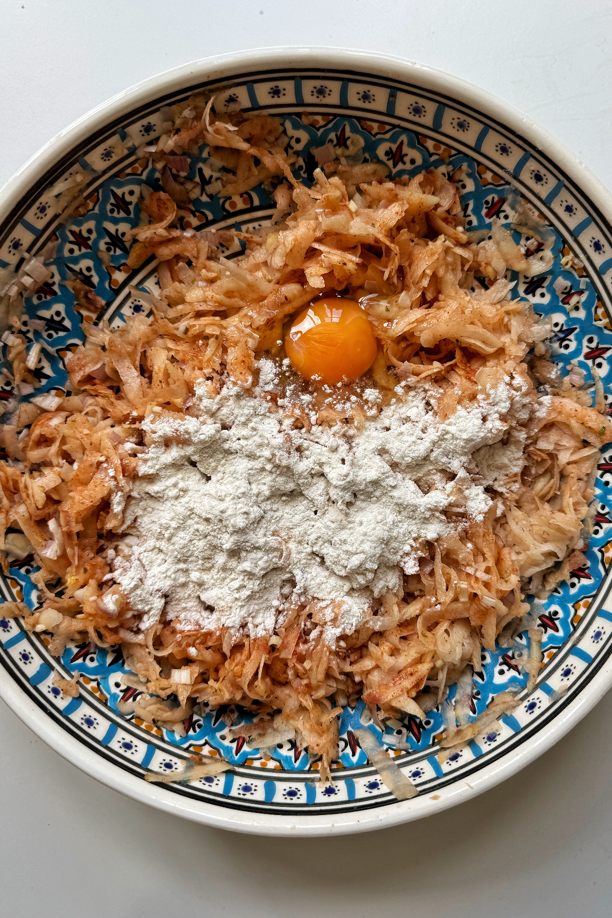 Grated potato with seasonings, flour, and egg in a bowl.