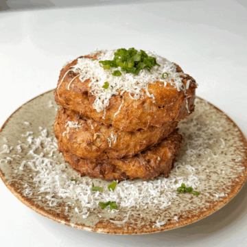 Air fryer hash browns stacked on a plate topped with parmesan and chives.