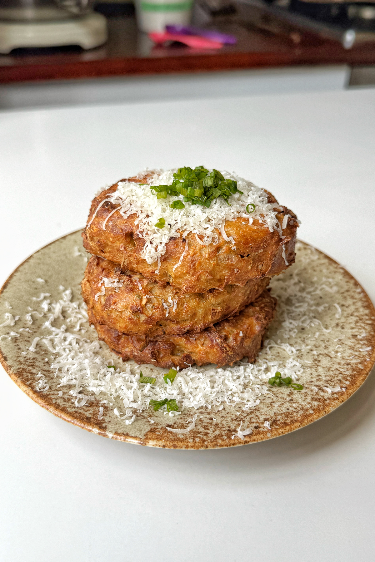 Air fryer hash browns stacked on a plate topped with parmesan and chives.