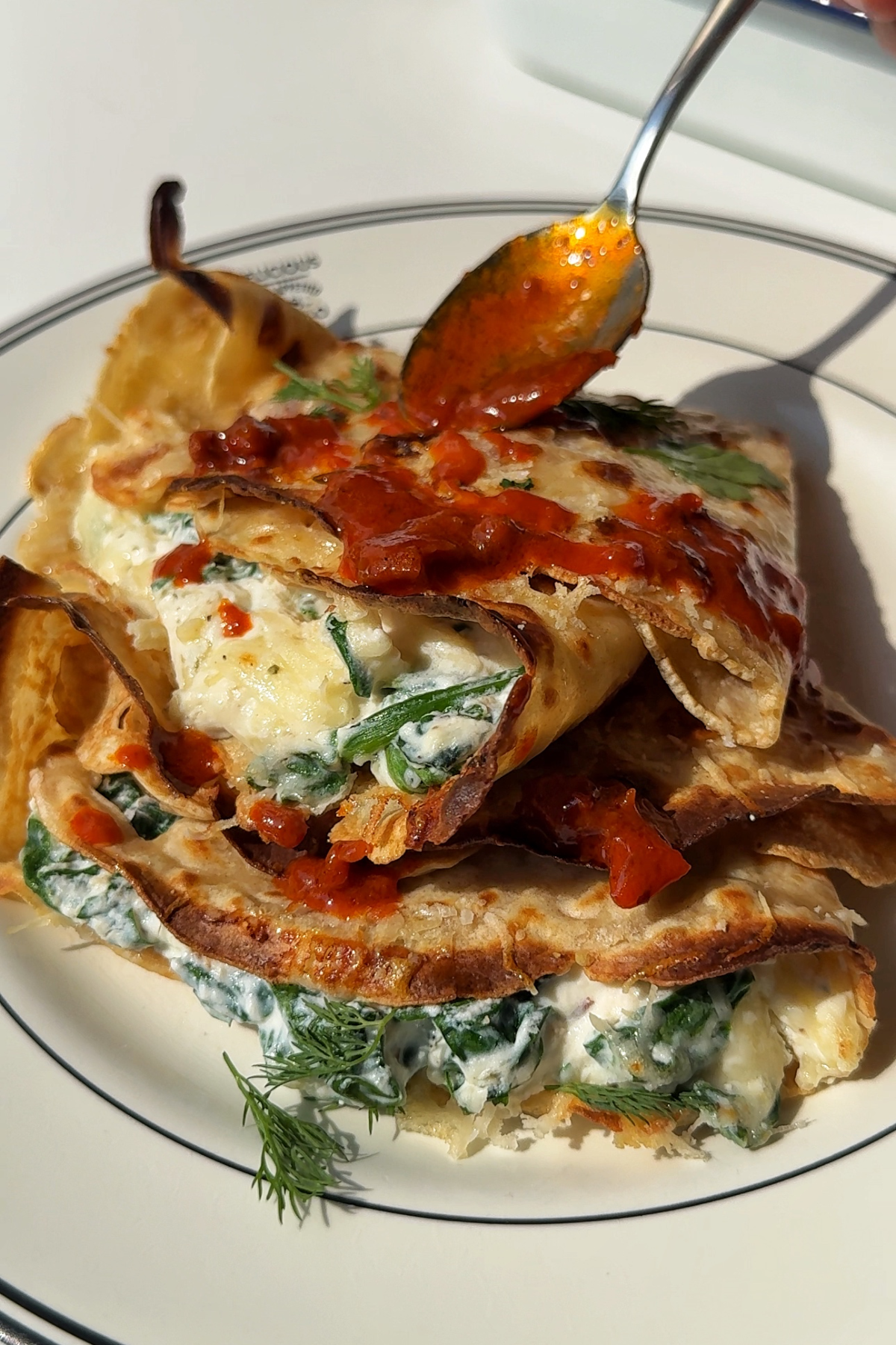 Drizzling hot harissa butter over the spinach and ricotta crespelle.