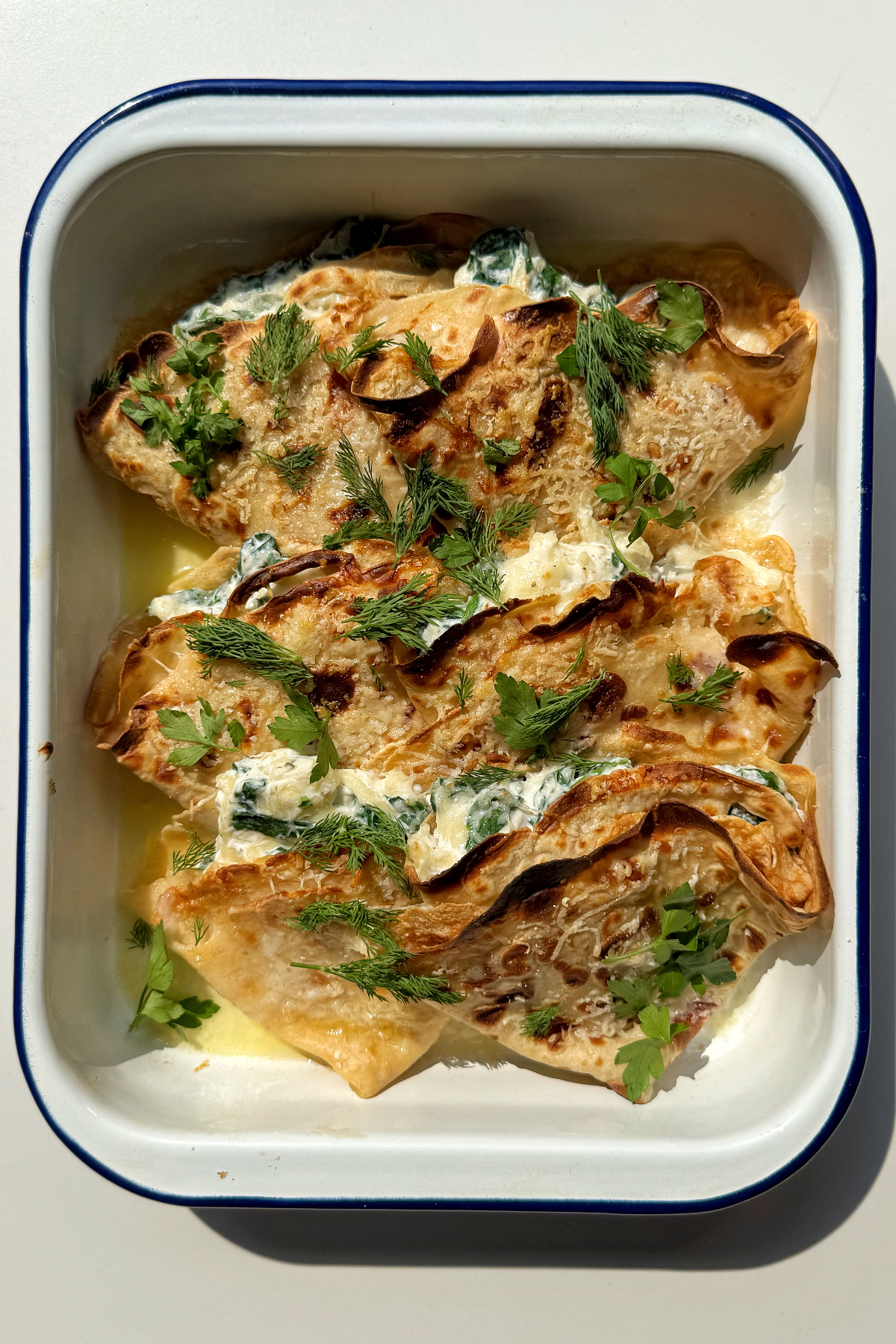 Crespelle in baking dish topped with dill and parsley.