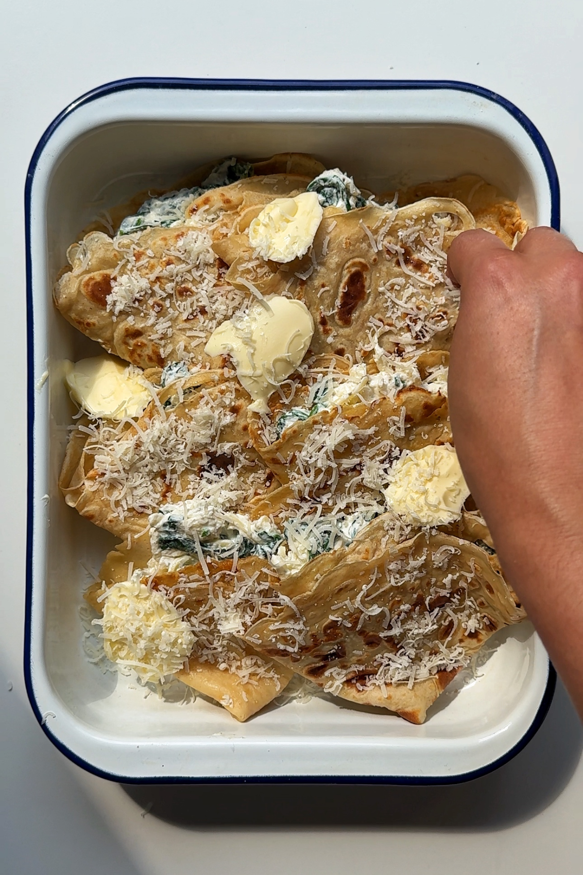 Stuffed pancakes in a baking dish topped with butter and parmesan.