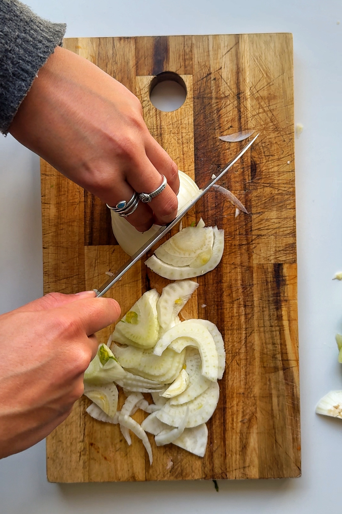 A hand slicing fennel on a wooden chopping board
