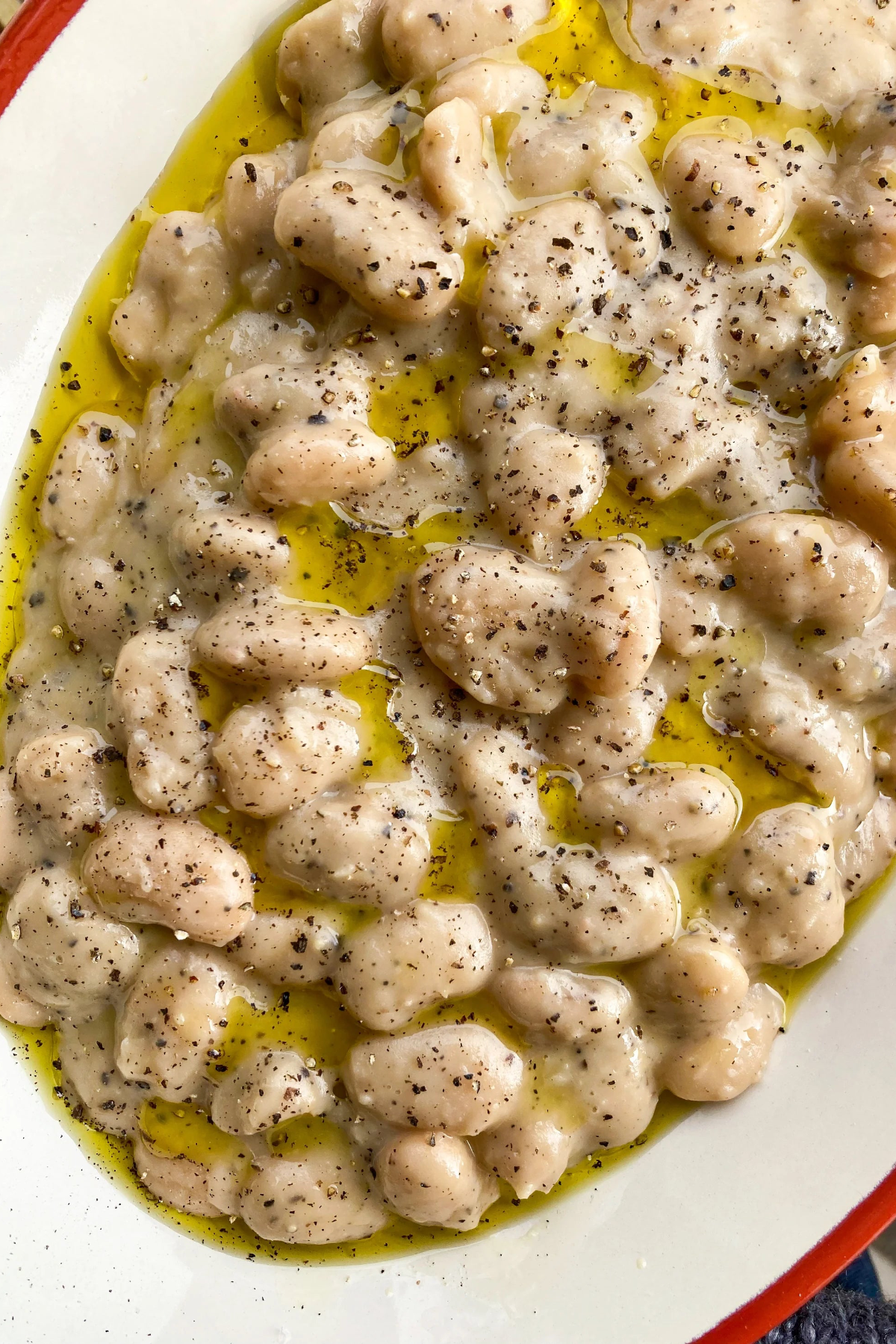butter beans in a cacio e pepe sauce on a white plate.