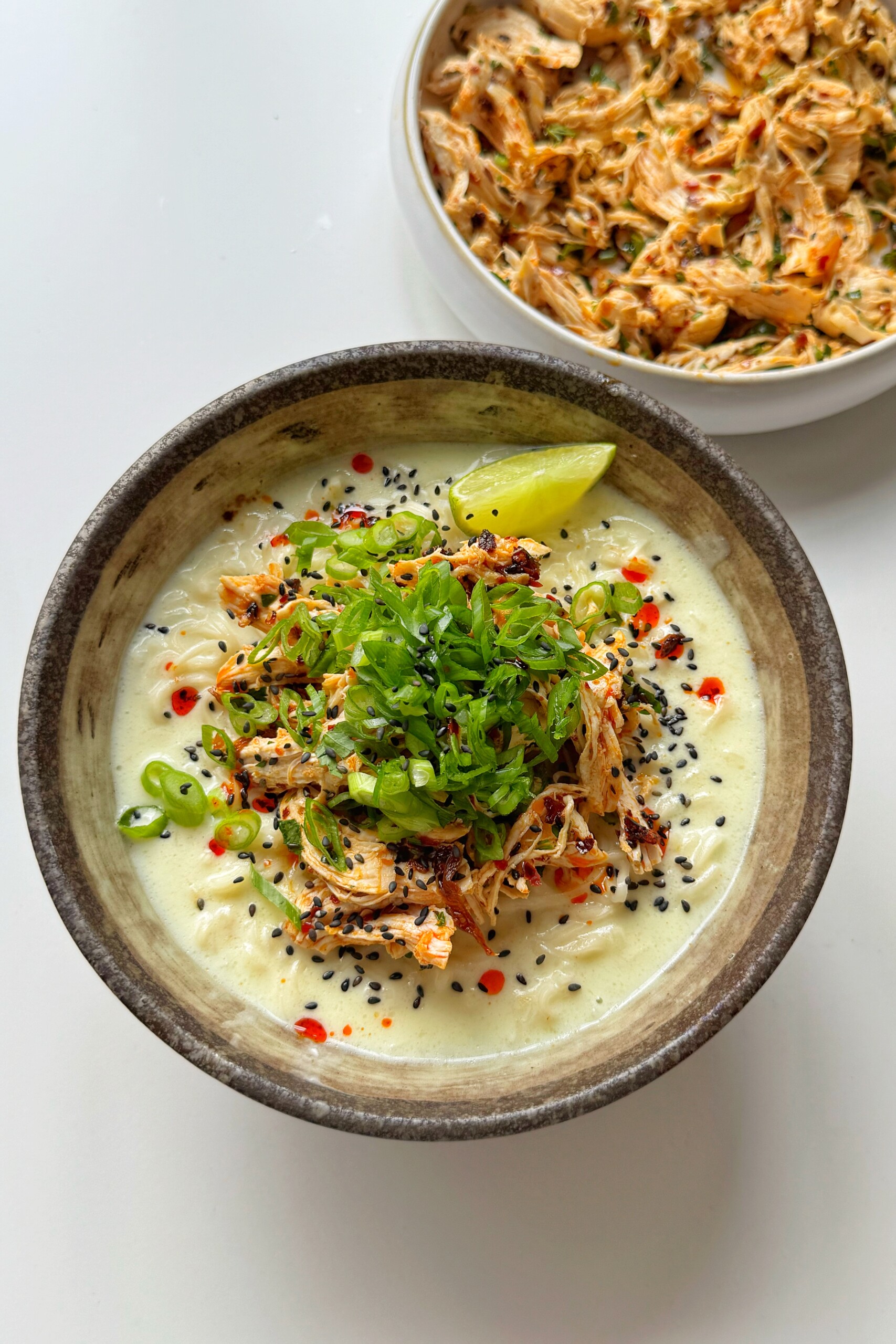 Lime and coconut chicken noodles in bowl on white surface.