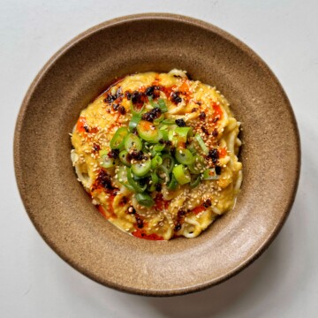 Miso corn noodles in brown bowl topped with spring onions and chili oil.