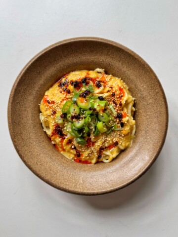 Miso corn noodles in brown bowl topped with spring onions and chili oil.