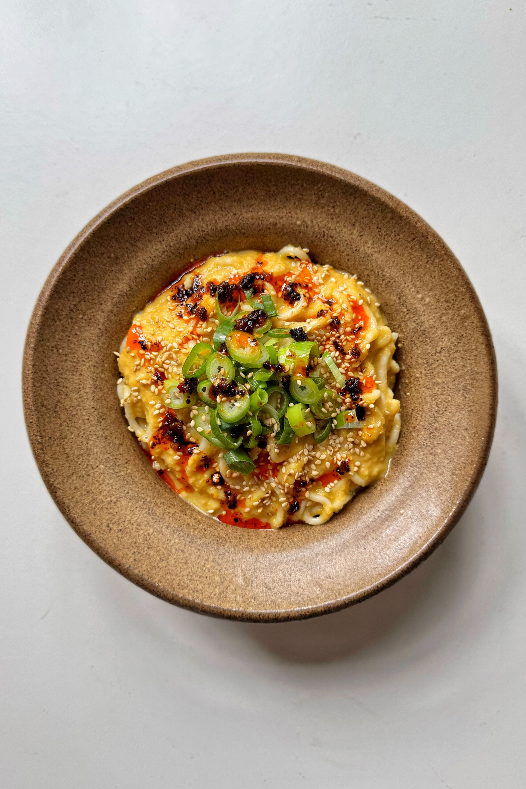 Miso corn noodles in brown bowl topped with spring onions and chili oil.