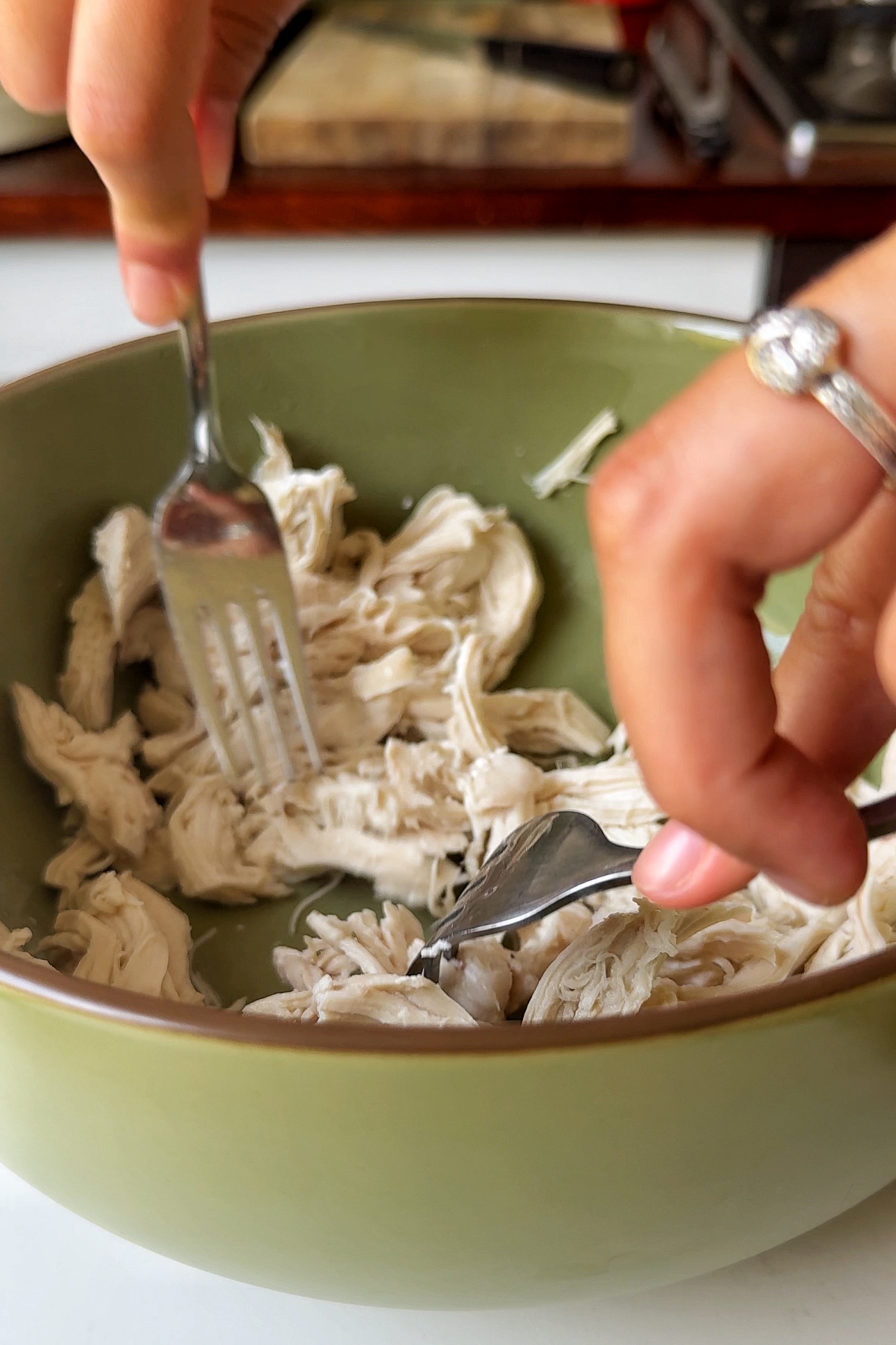 Shredding chicken in a green bowl.