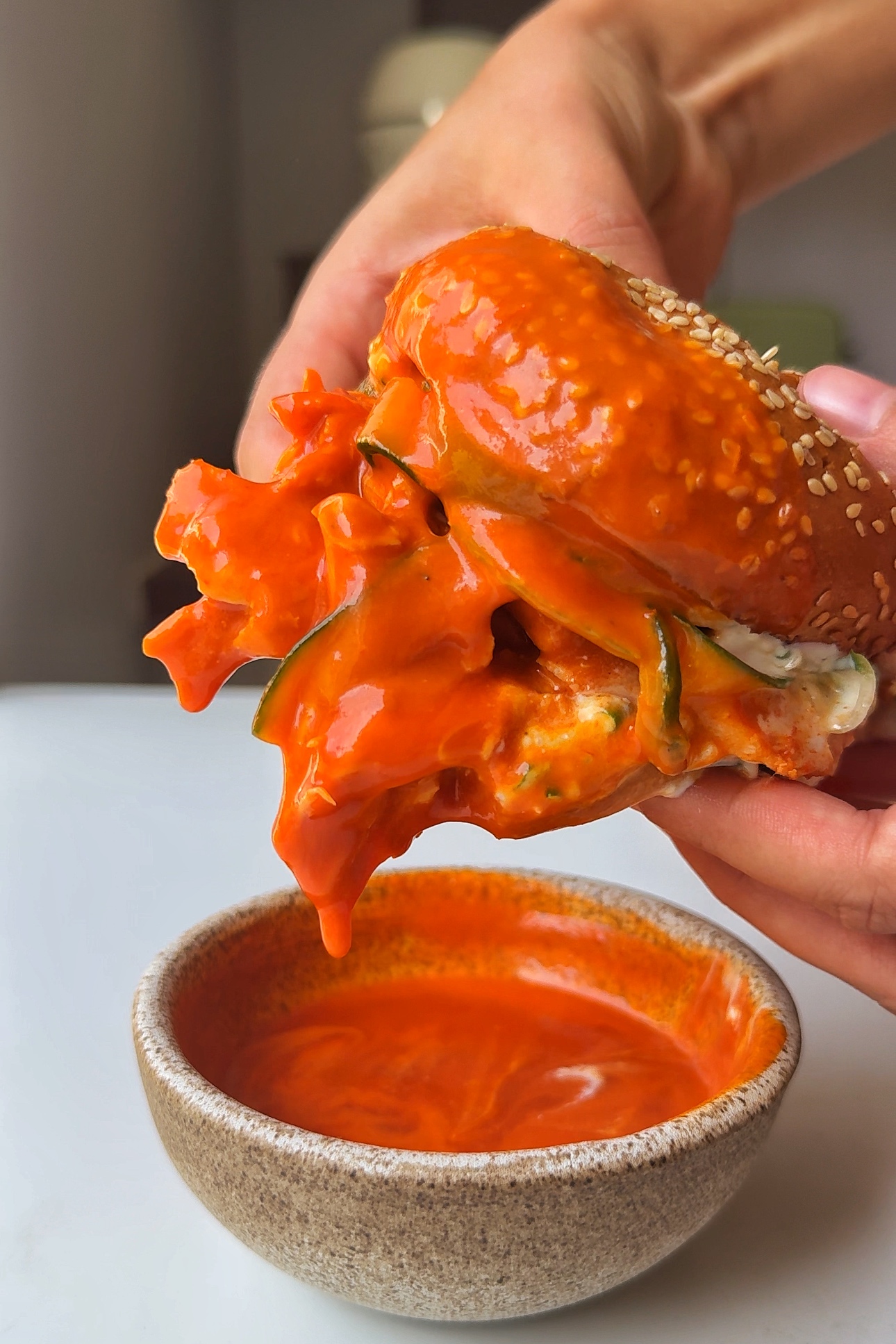 Dipping buffalo chicken sandwich in buffalo sauce.