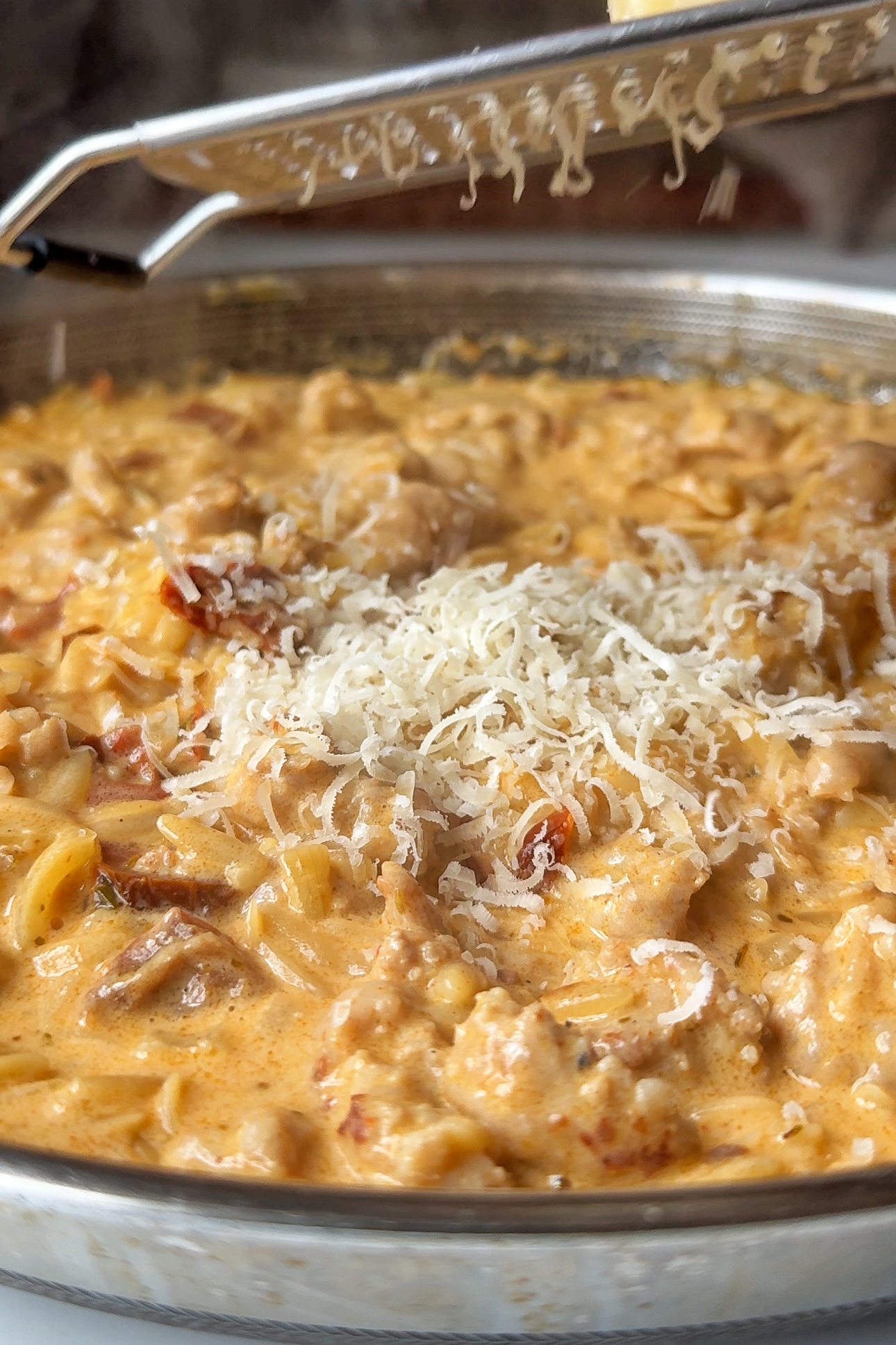 Adding parmesan into sausage orzotto dish.