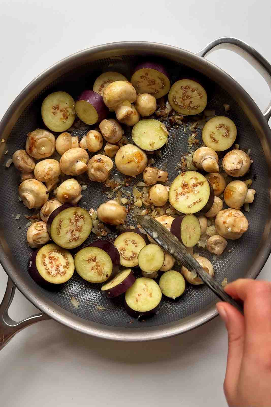 Frying aubergine with button mushrooms in a pan.