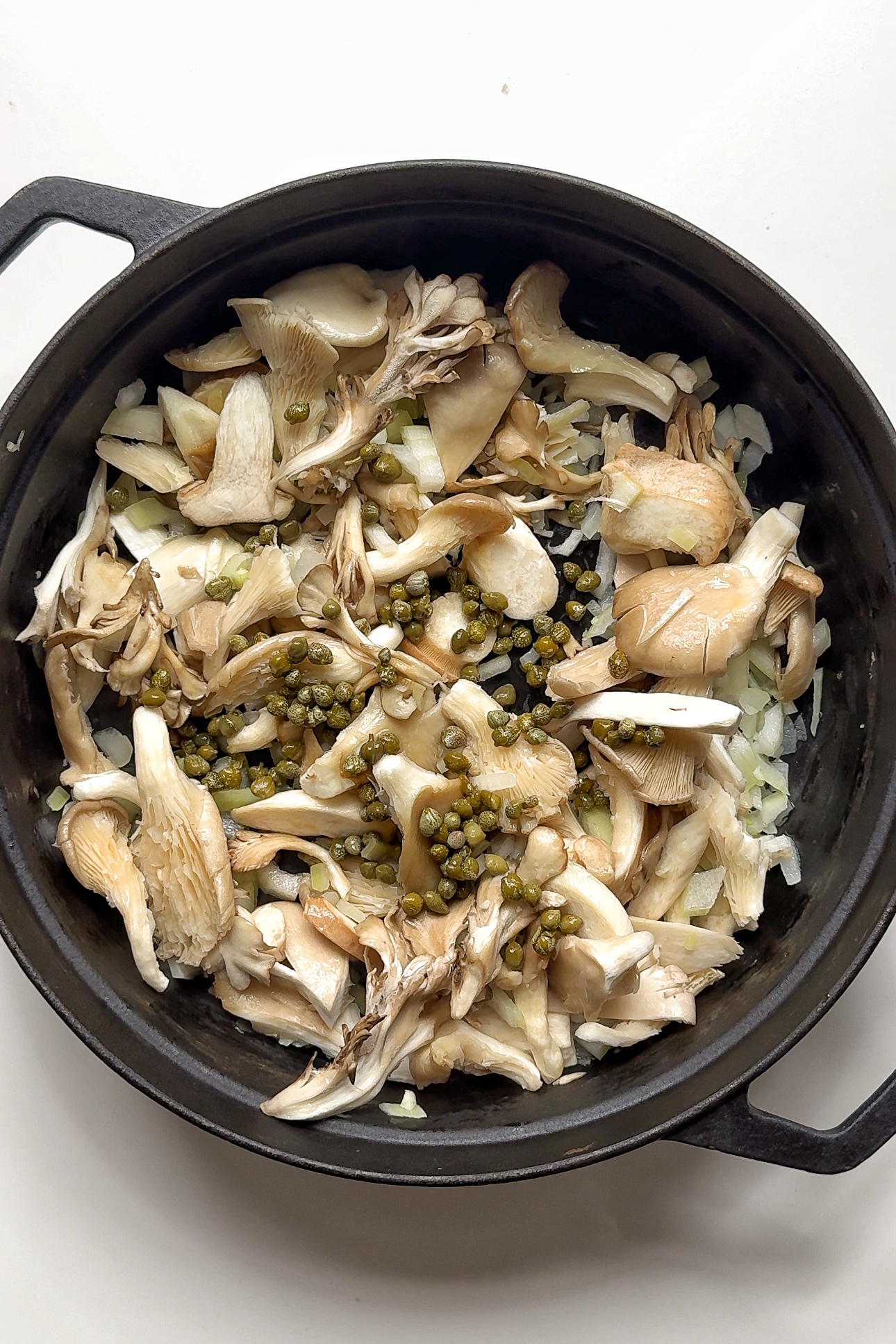 frying off mushrooms and capers in a black pan.