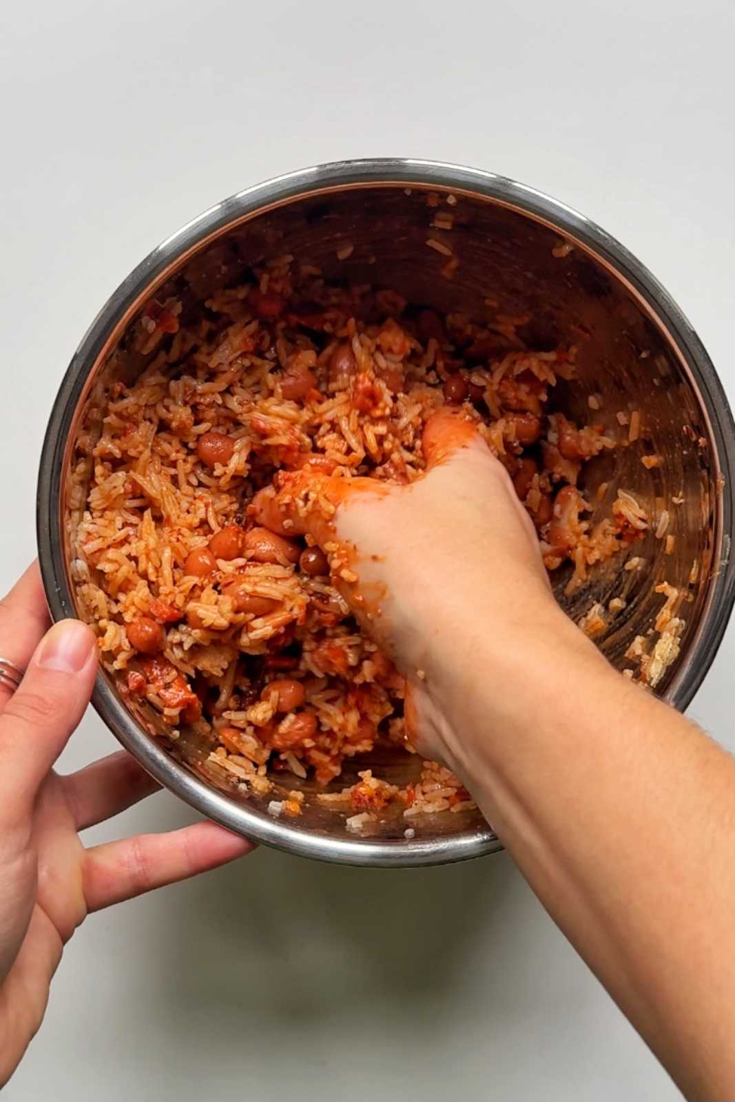 Mashing up rice and beans in a metal bowl.