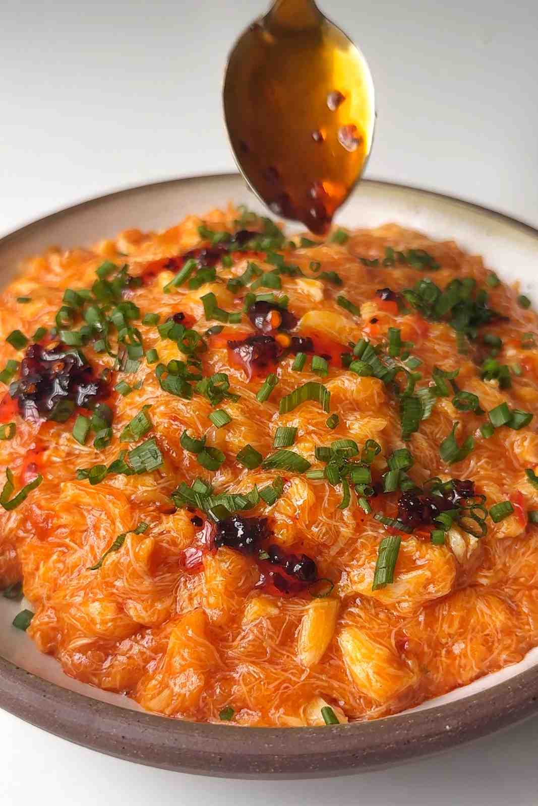 Pouring chilli crisp on chilli crab noodles.