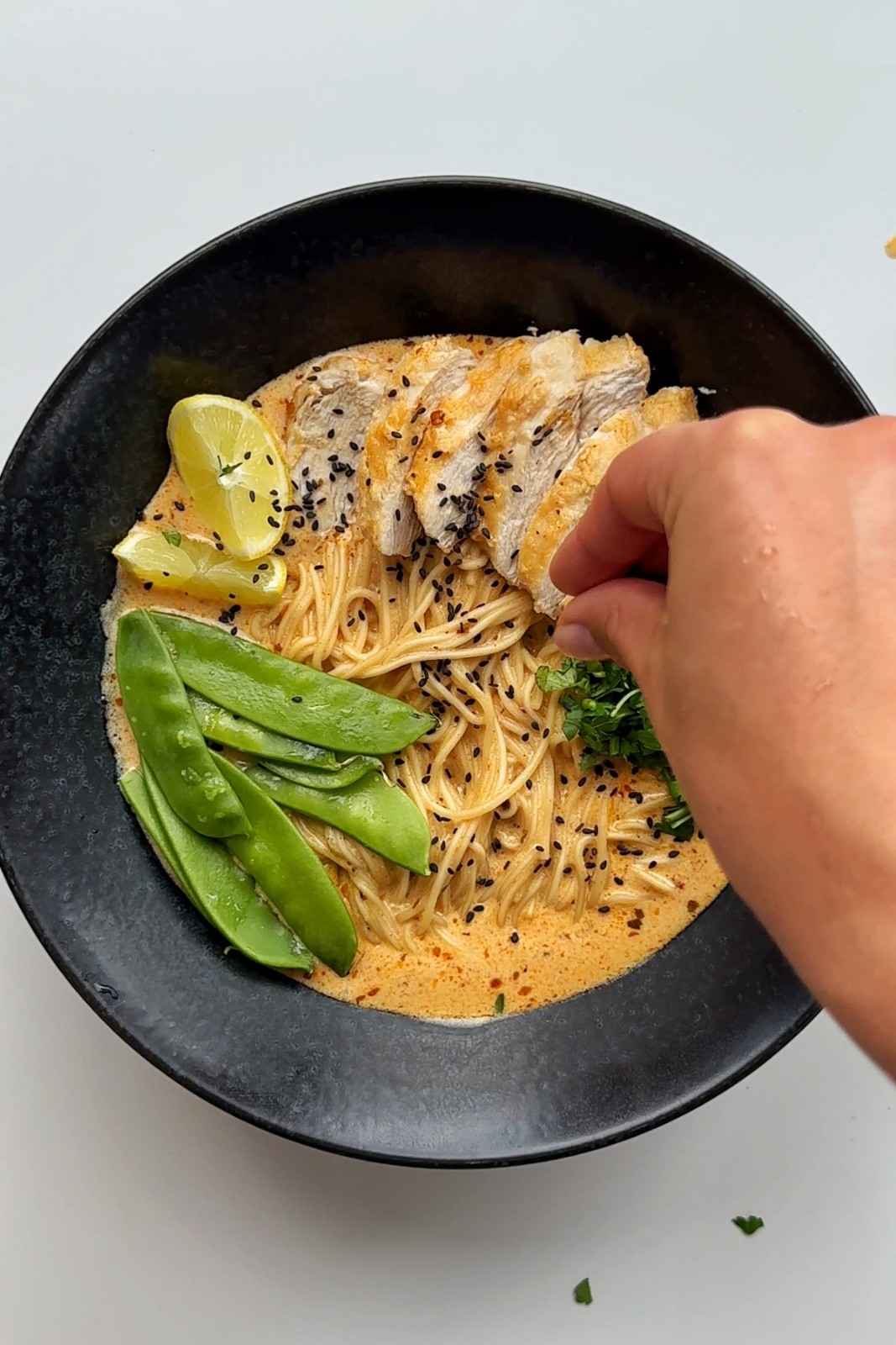A handful of mangetout (snow peas) on top of a bowl of lemon ramen
